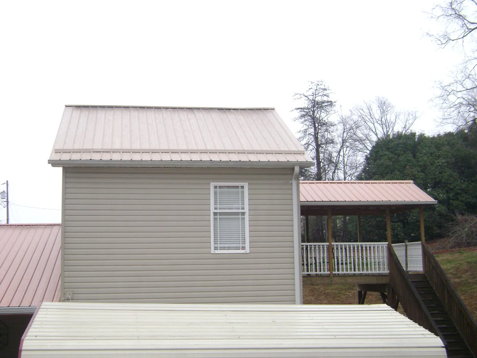 Tan metal roofs on a two story addition and attached porch, from a Roof Replacement job in Hobart